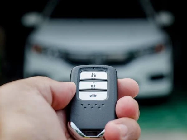 Driver holding a car key fob in front of a car